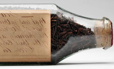 Glass bottle full of dry tea leaves positioned on its side so the handwritten label is visible